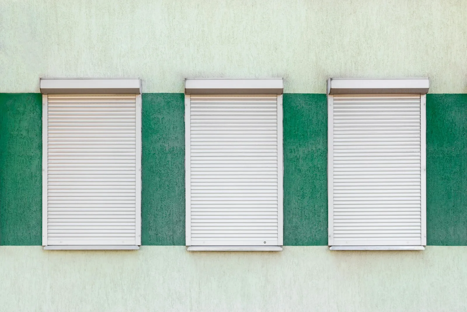 Drei Fenster mit weißen Rolläden an einer Hausfassade